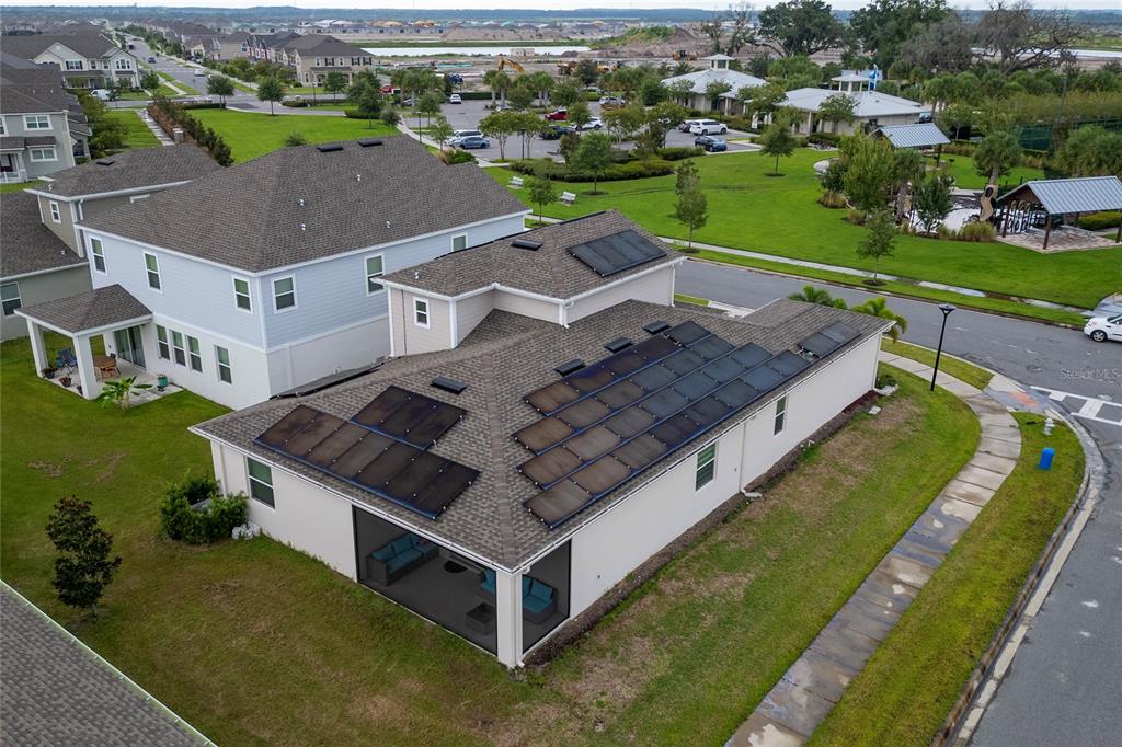 An aerial view shows a house with solar panels on the roof and a screened-in patio — 1839 GOOD NEIGHBOR LOOP, KISSIMMEE, FL