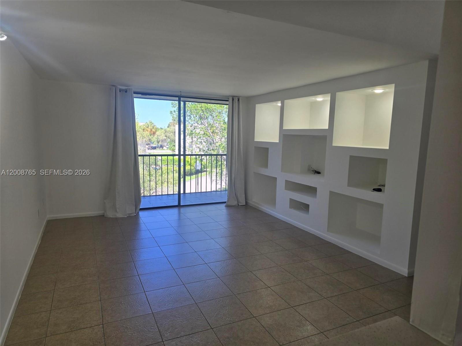 An empty room features tile flooring, a sliding glass door to a balcony, and built-in shelving — 8045 SW 107th Ave # 323, Miami FL 33173, MIAMI, FL