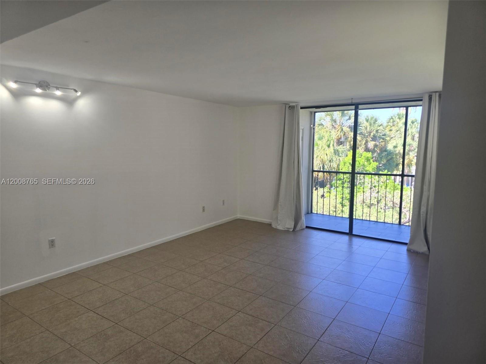 An empty room features beige tile flooring, white walls, a track light, and a balcony — 8045 SW 107th Ave # 323, Miami FL 33173, MIAMI, FL