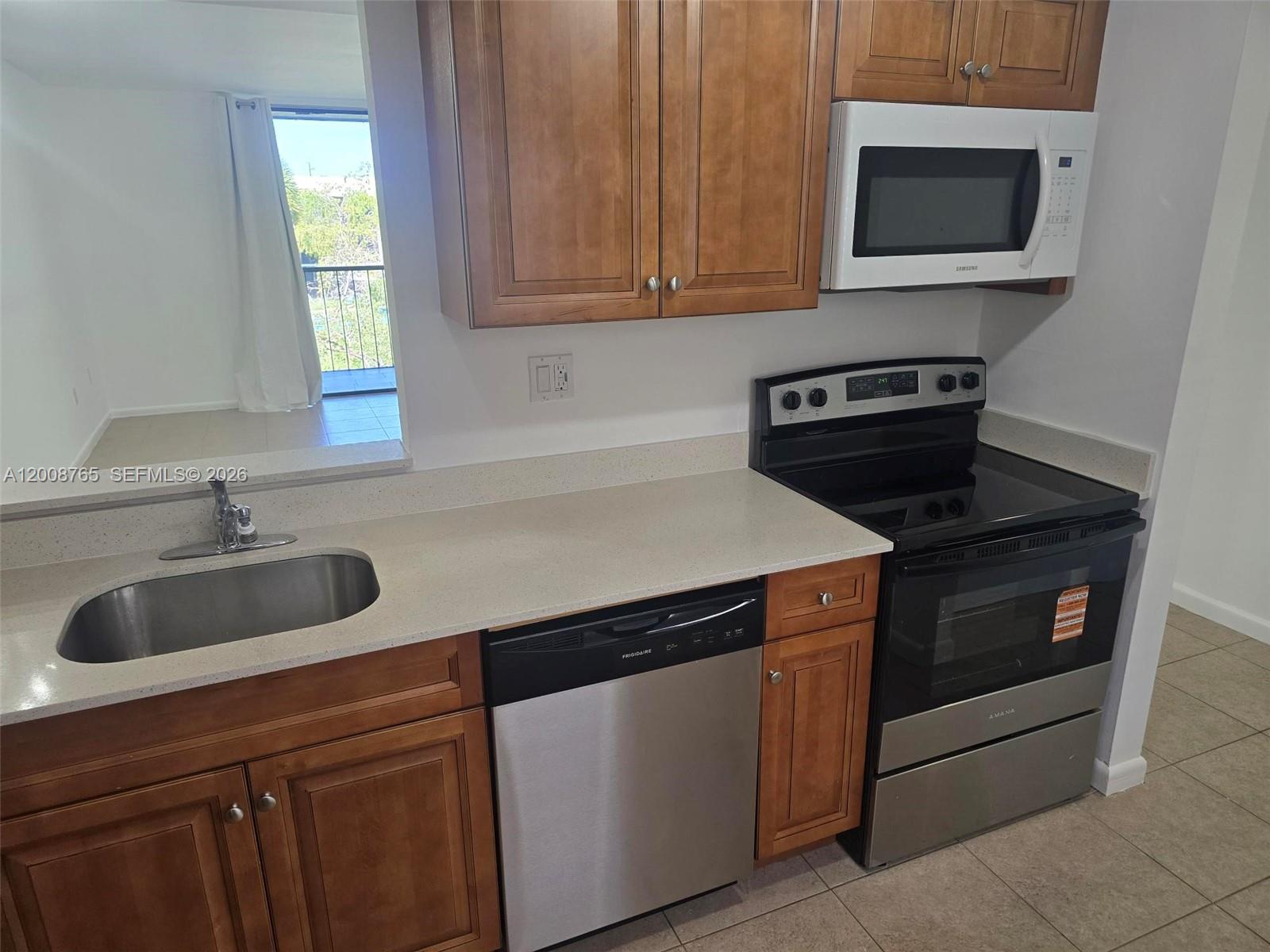 A kitchen features wood cabinets, stainless steel appliances, and a view of a balcony — 8045 SW 107th Ave # 323, Miami FL 33173, MIAMI, FL