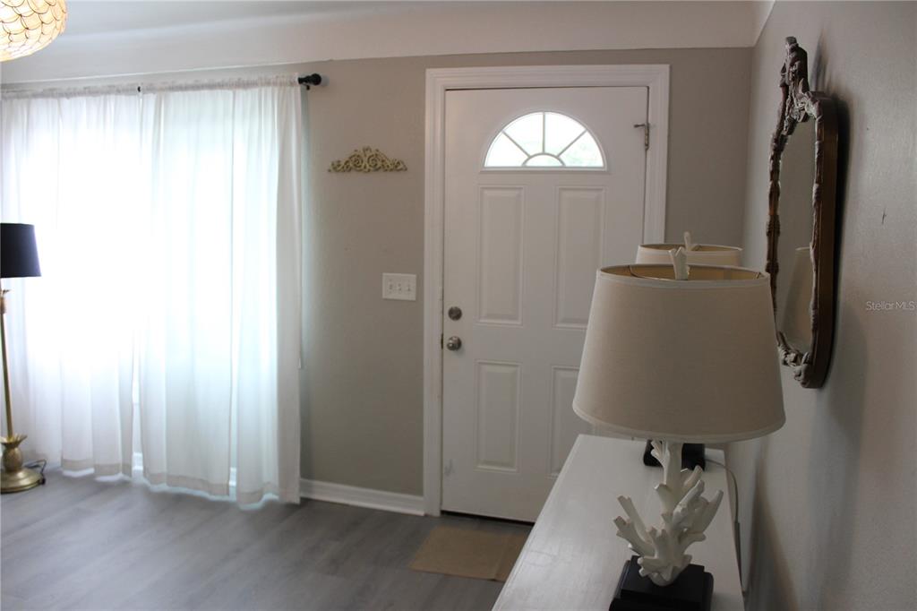 An entryway features a white front door, light-colored flooring, and a decorative table lamp — 6014 CEDAR STREET NE, ST PETERSBURG, FL