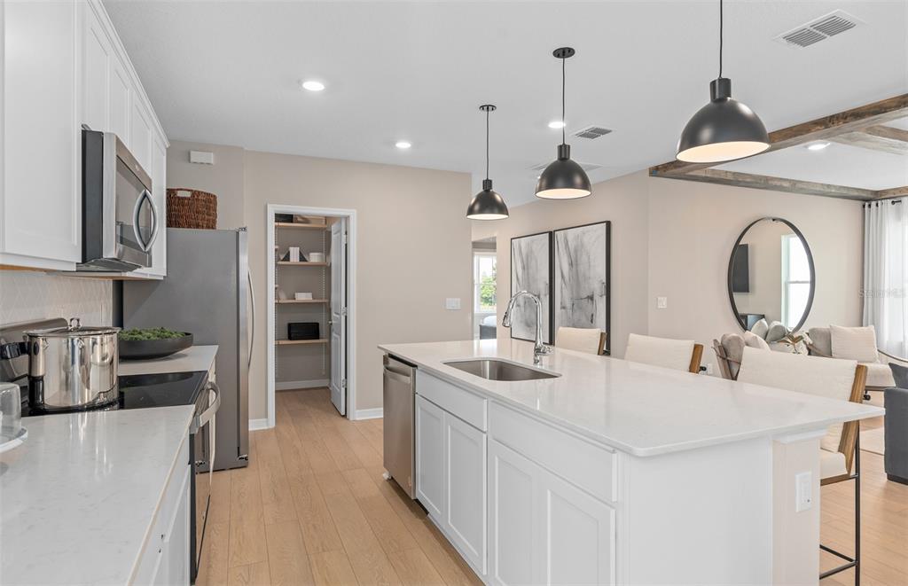 A modern kitchen features white cabinetry, a quartz-topped island, stainless steel appliances, and wood flooring — 2290 GROW BOULEVARD, ORLANDO, FL