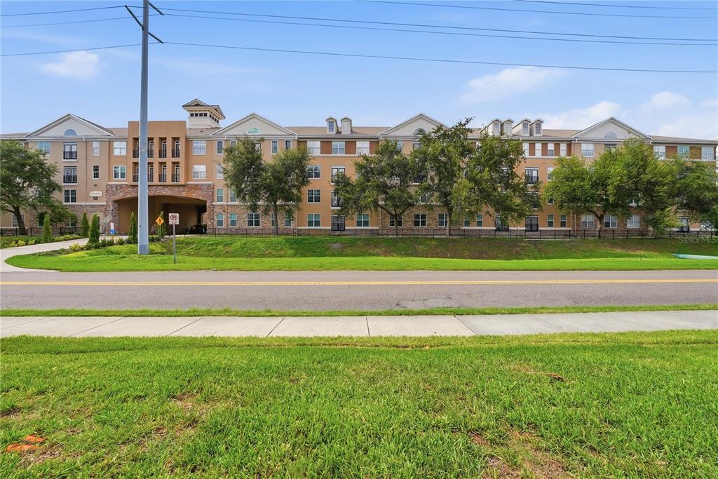 A multi-story apartment building with a stone-accented entrance stands behind a grassy lawn — 4221 W SPRUCE STREET UNIT 2203, TAMPA, FL