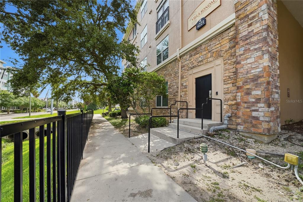 A stone-faced apartment building entrance with a black door and metal handrails along a sidewalk — 4221 W SPRUCE STREET UNIT 2203, TAMPA, FL