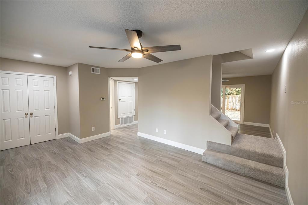 A room with gray wood-look flooring, a ceiling fan, and stairs leading to a doorway — 740 N FAIRFIELD DRIVE, PENSACOLA, FL