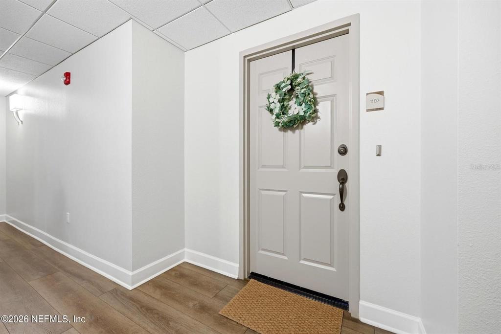 A hallway features wood-look flooring, white walls, a drop ceiling, and a door numbered 1107 — 1478 RIVERPLACE BOULEVARD UNIT 1107, JACKSONVILLE, FL