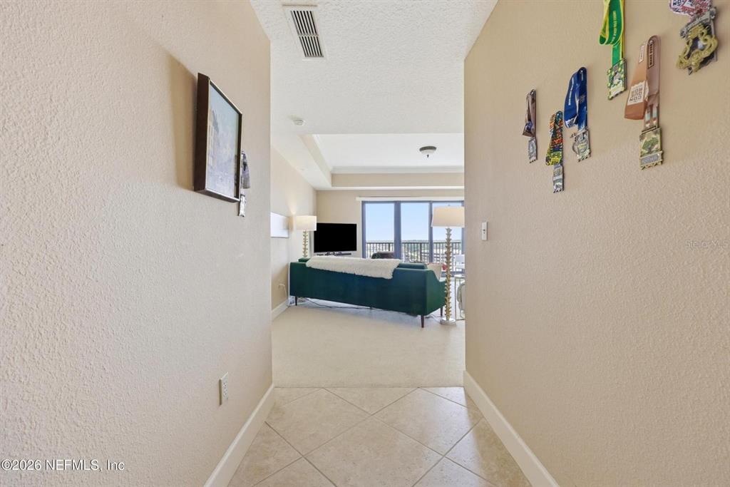 A tiled entryway leads into a carpeted living room with a green sofa and balcony — 1478 RIVERPLACE BOULEVARD UNIT 1107, JACKSONVILLE, FL