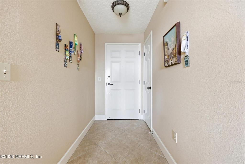 A tiled entryway features a white front door, beige walls, and wall-mounted race medals — 1478 RIVERPLACE BOULEVARD UNIT 1107, JACKSONVILLE, FL