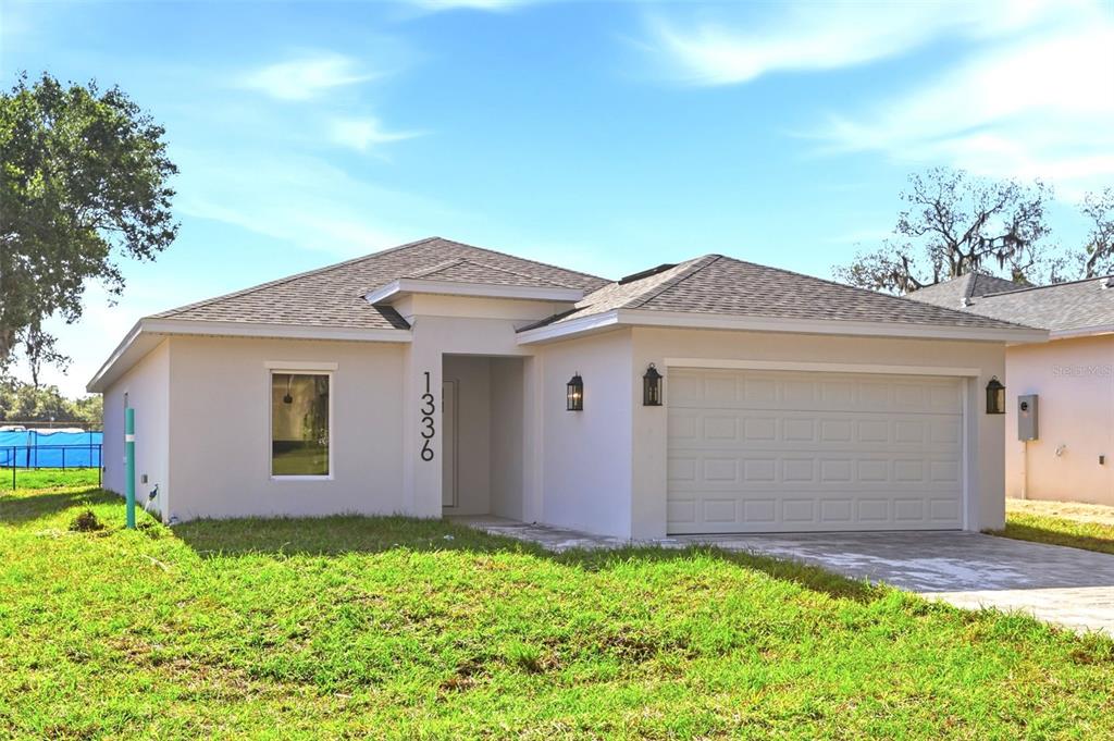 A single-story house with a white stucco exterior, a two-car garage, and a front lawn — 1336 MARSHALL DRIVE, LEESBURG, FL