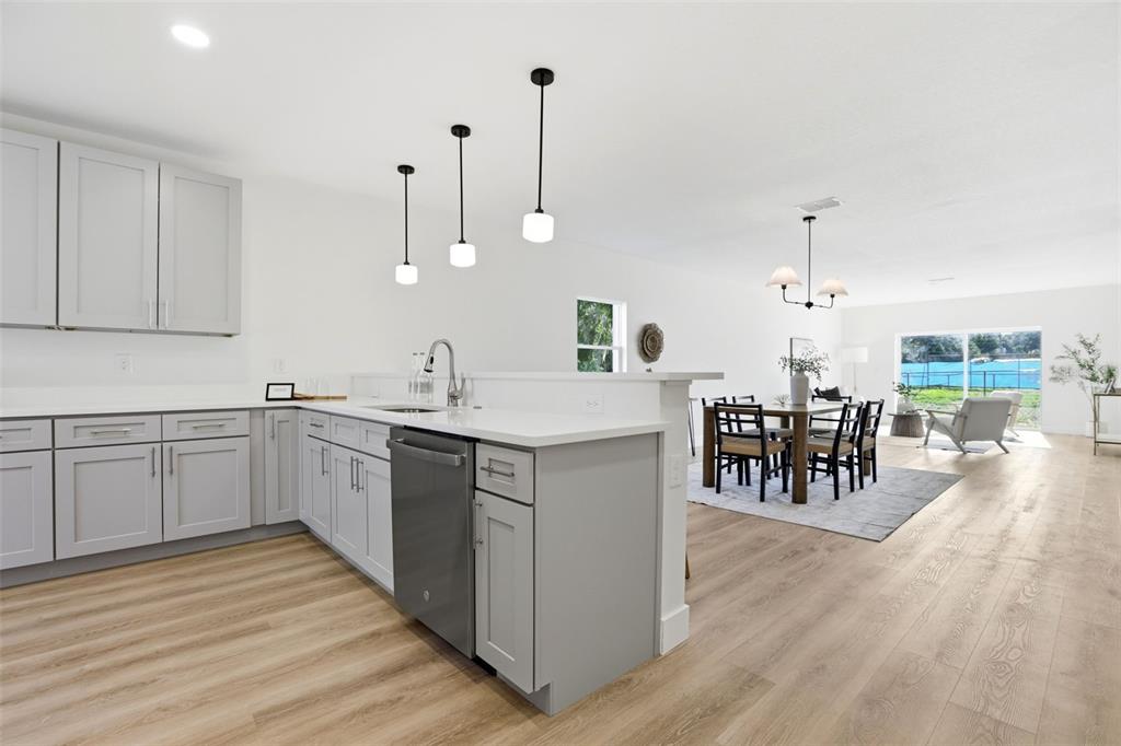 A kitchen with gray cabinets and white countertops overlooks an open-concept dining and living area — 1336 MARSHALL DRIVE, LEESBURG, FL