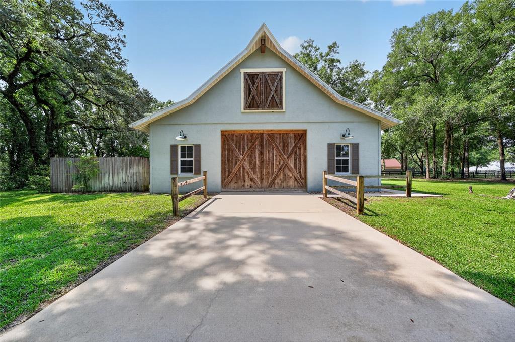 A light-colored barn-style garage with wooden double doors and a loft window sits outdoors — 7040 SW 97TH PLACE, OCALA, FL