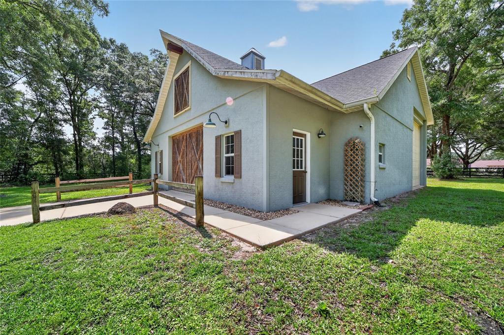 A light green barn-style building with wooden sliding doors, a side entrance, and a fence — 7040 SW 97TH PLACE, OCALA, FL