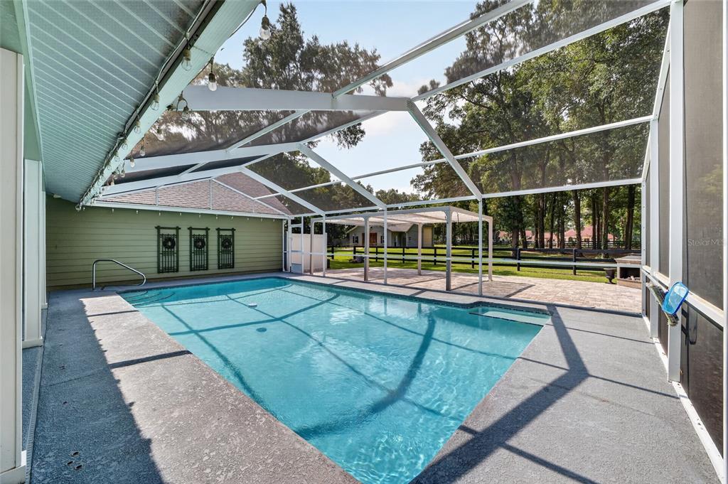A screened-in swimming pool with a concrete deck and a covered patio area — 7040 SW 97TH PLACE, OCALA, FL