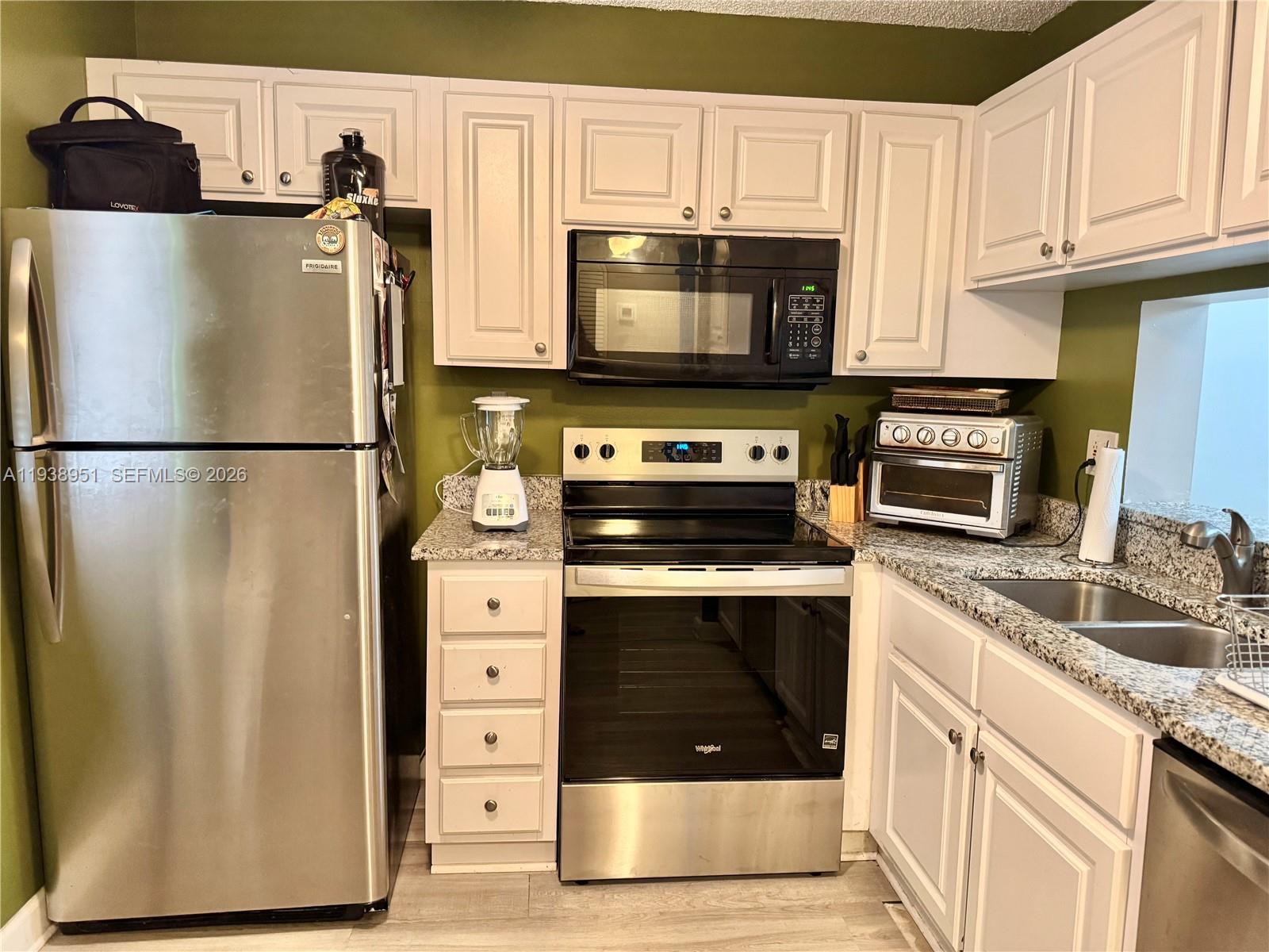 A kitchen features white cabinets, stainless steel appliances, granite countertops, and olive green walls — 5580 Lakeside Dr # 205, Margate FL 33063, MARGATE, FL
