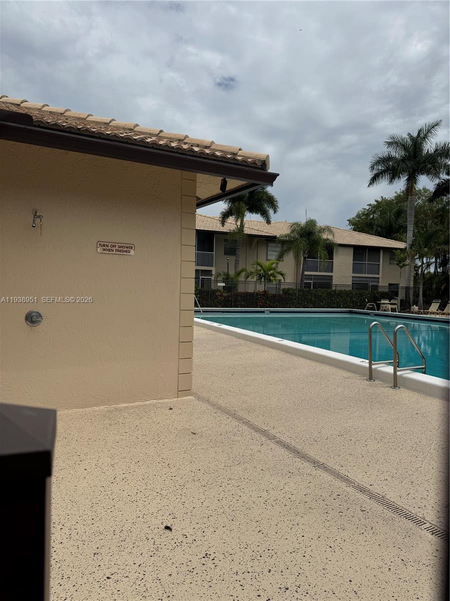 A swimming pool sits next to a building with an outdoor shower and palm trees — 5580 Lakeside Dr # 205, Margate FL 33063, MARGATE, FL