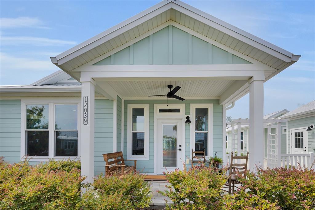 A light blue house features a covered front porch with a ceiling fan and rockers — 12039 LAKESHORE WAY, OXFORD, FL