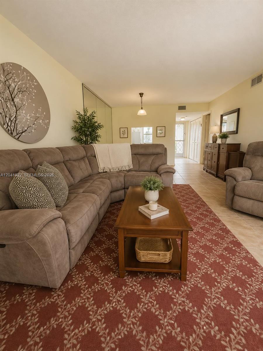 A living room features a large brown sectional sofa, a coffee table, and tile flooring — 20 Abbey Ln # 101, Delray Beach FL 33446, DELRAY BEACH, FL