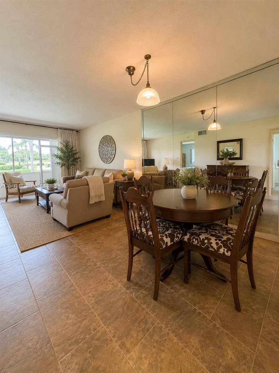 A dining area with a round wooden table sits adjacent to a living room — 20 Abbey Ln # 101, Delray Beach FL 33446, DELRAY BEACH, FL