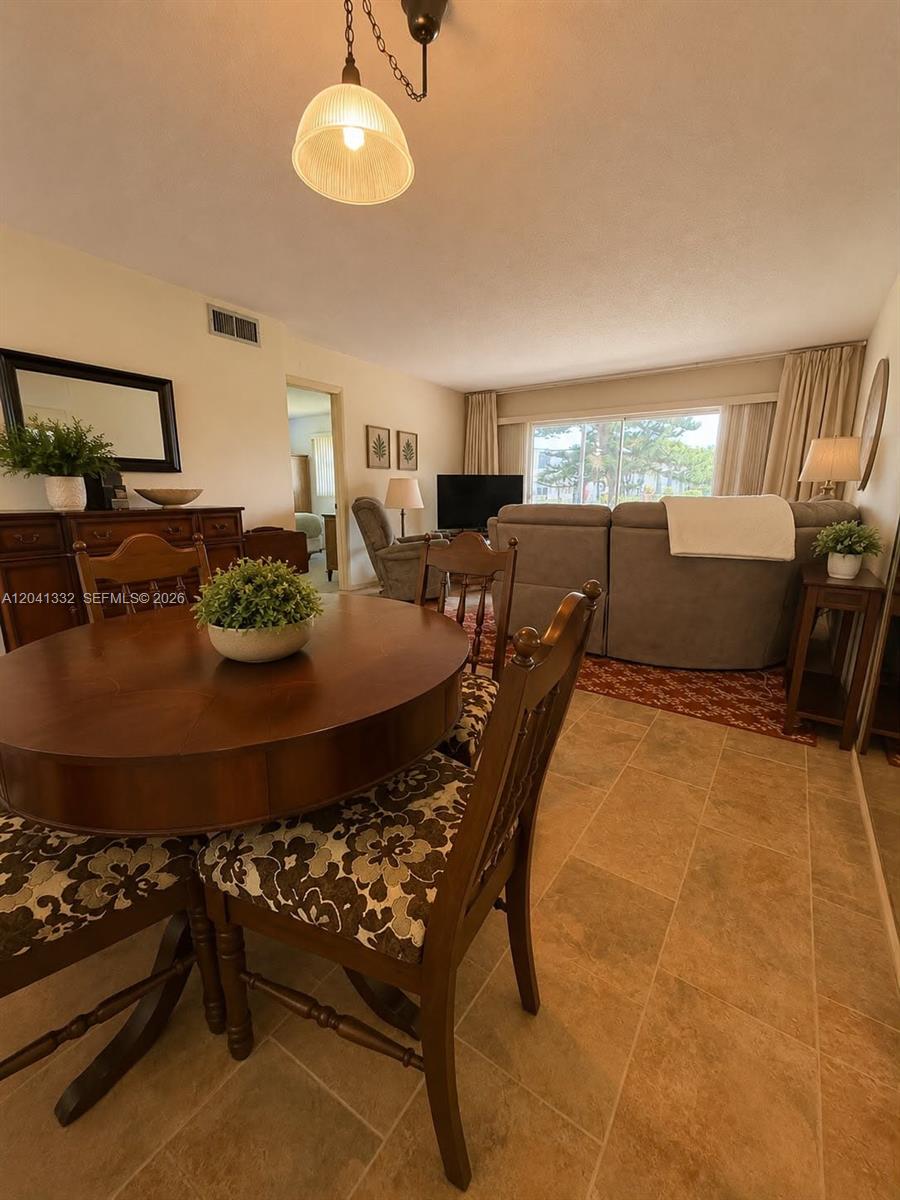A dining area with a round wooden table leads into a living room with tile floors — 20 Abbey Ln # 101, Delray Beach FL 33446, DELRAY BEACH, FL
