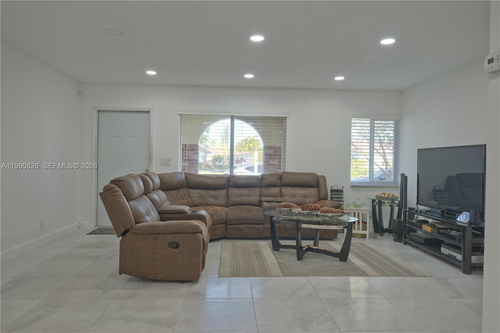 A living room features a brown sectional sofa, glass coffee table, and tile flooring — 4391 NW 12th Ter, Deerfield Beach FL 33064, DEERFIELD BEACH, FL