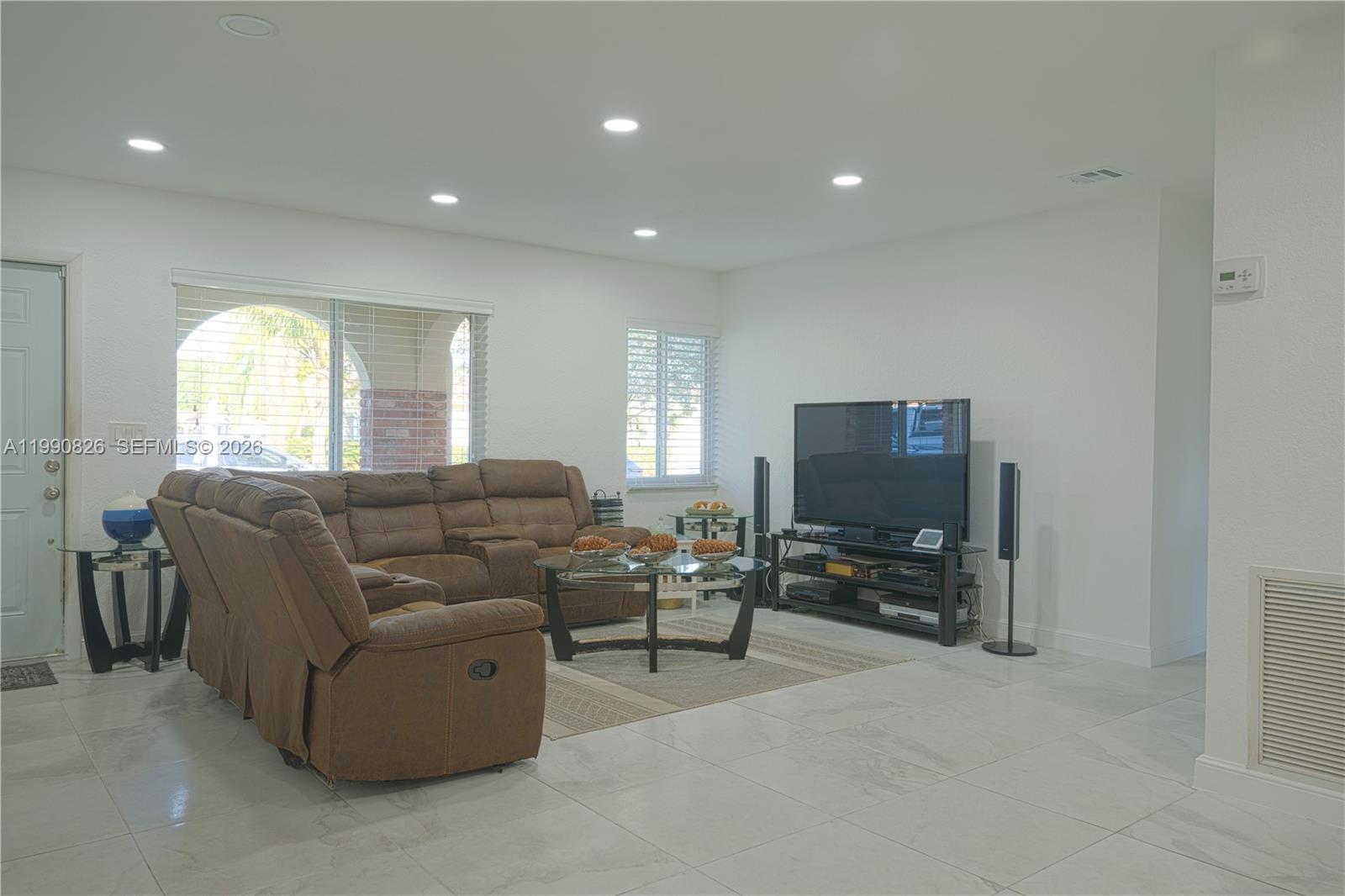 A living room features a brown sectional sofa, a glass coffee table, and tile flooring — 4391 NW 12th Ter, Deerfield Beach FL 33064, DEERFIELD BEACH, FL