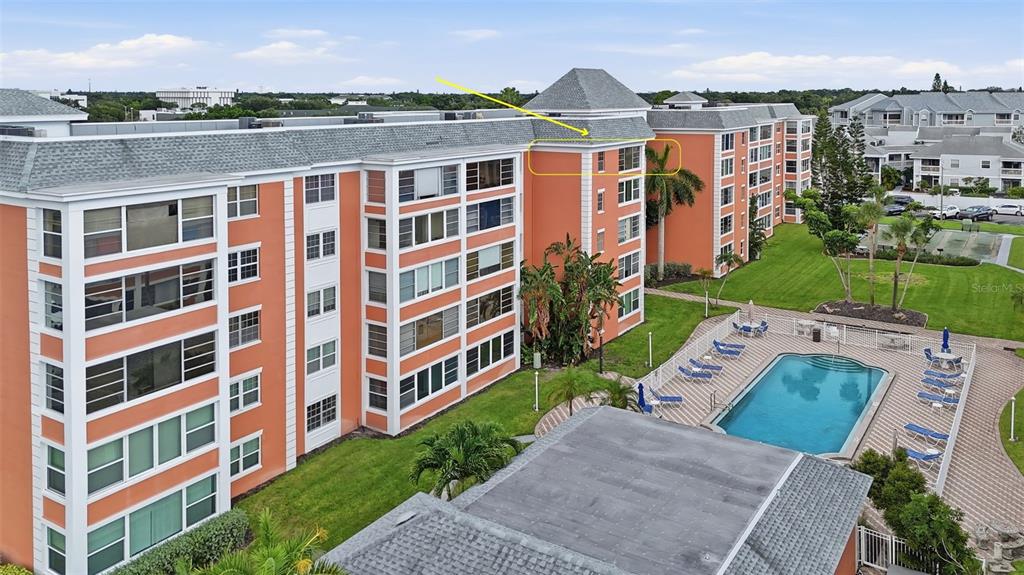 An aerial view of a multi-story orange apartment building with a swimming pool below — 6800 20TH AVENUE N UNIT 505, ST PETERSBURG, FL