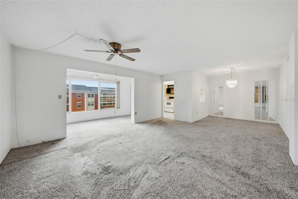 An empty living room features gray wall-to-wall carpeting, a ceiling fan, and a large window — 6800 20TH AVENUE N UNIT 505, ST PETERSBURG, FL