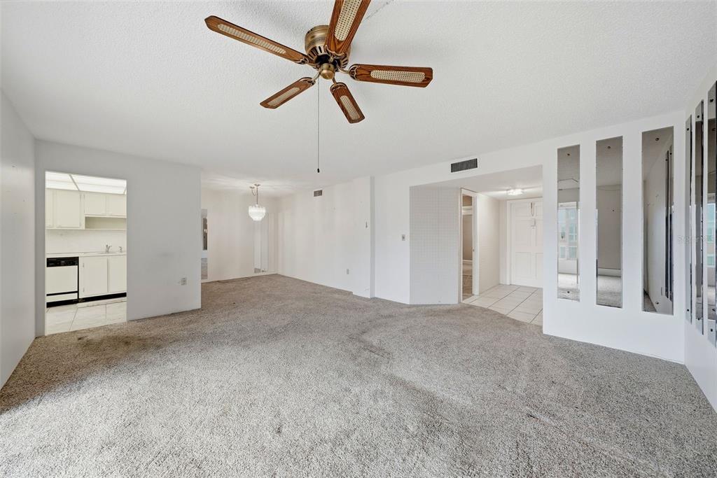 A living room with gray carpet, a ceiling fan, and vertical mirror panels on the wall — 6800 20TH AVENUE N UNIT 505, ST PETERSBURG, FL