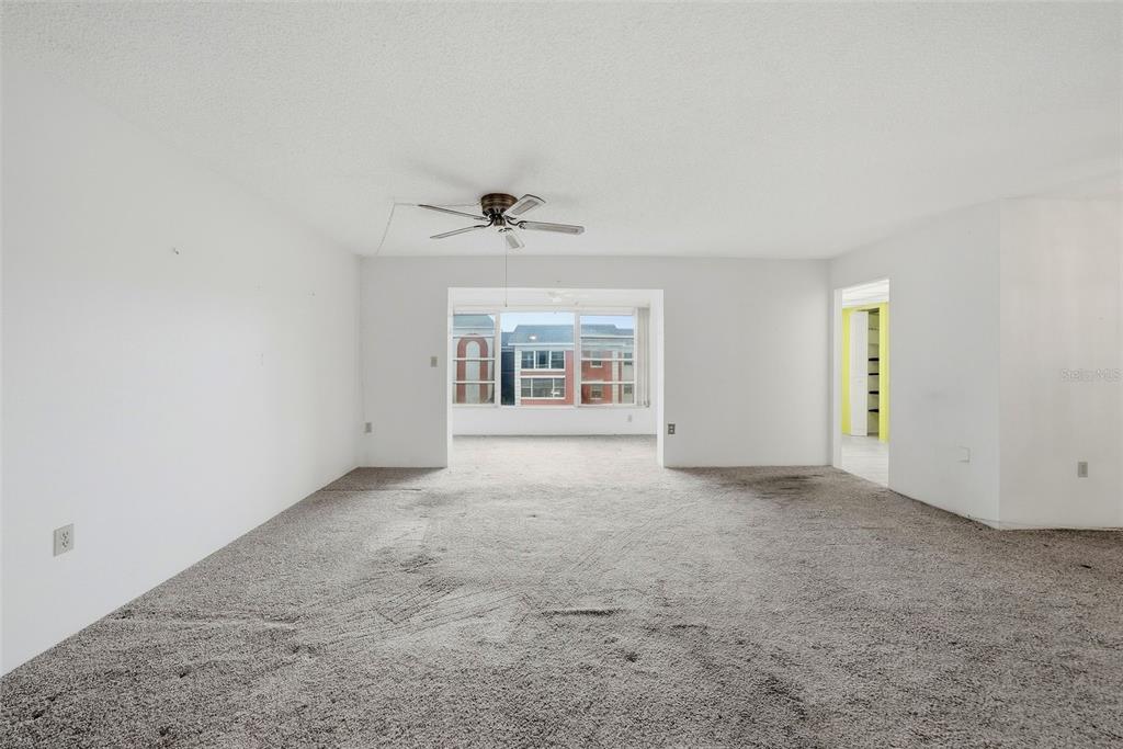 An empty living room features gray carpeting, white walls, a ceiling fan, and large windows — 6800 20TH AVENUE N UNIT 505, ST PETERSBURG, FL
