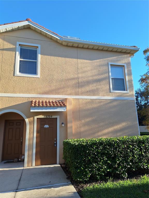 A two-story tan stucco building features a brown front door and a manicured hedge — 3709 PARKRIDGE CIRCLE UNIT 7-204, SARASOTA, FL