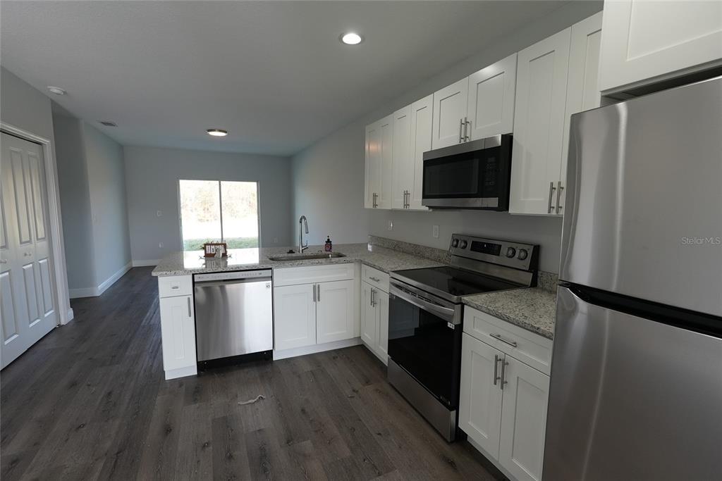 A kitchen features white cabinets, stainless steel appliances, granite countertops, and dark wood-look flooring — 17196 BONNIE AVENUE, PORT CHARLOTTE, FL