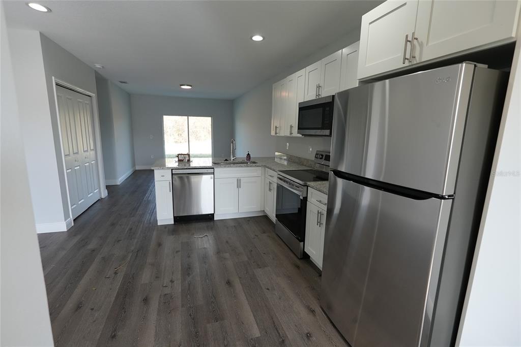 A modern kitchen features white cabinets, stainless steel appliances, granite countertops, and gray wood flooring — 17196 BONNIE AVENUE, PORT CHARLOTTE, FL