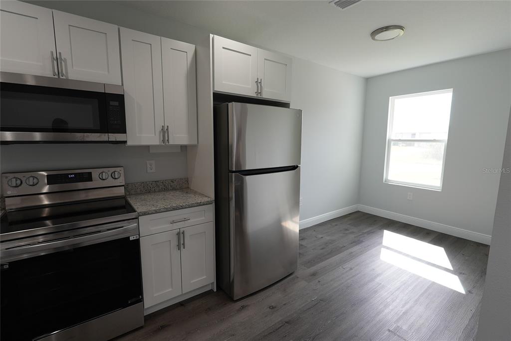 A kitchen features white cabinets, stainless steel appliances, granite countertops, and wood-look flooring — 17196 BONNIE AVENUE, PORT CHARLOTTE, FL