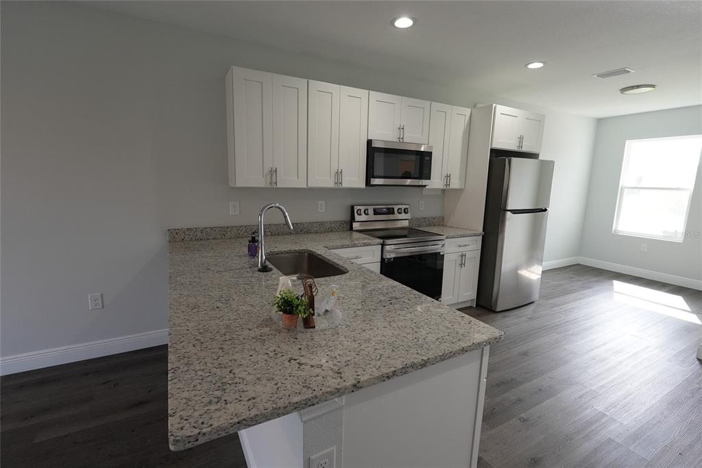 A kitchen features white cabinets, granite countertops, stainless steel appliances, and dark wood-look flooring — 17196 BONNIE AVENUE, PORT CHARLOTTE, FL