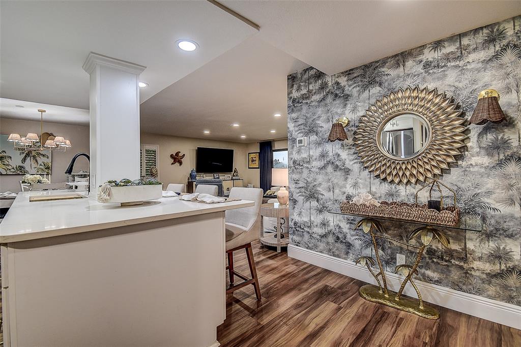 A kitchen island overlooks a living area featuring palm-patterned wallpaper and a gold sunburst mirror — 36750 US HIGHWAY 19 UNIT 24-213, PALM HARBOR, FL