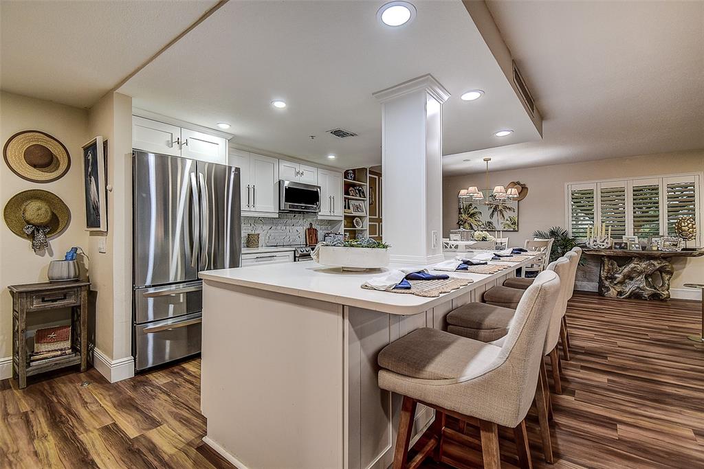A kitchen features a white island with bar seating, stainless steel appliances, and wood flooring — 36750 US HIGHWAY 19 UNIT 24-213, PALM HARBOR, FL