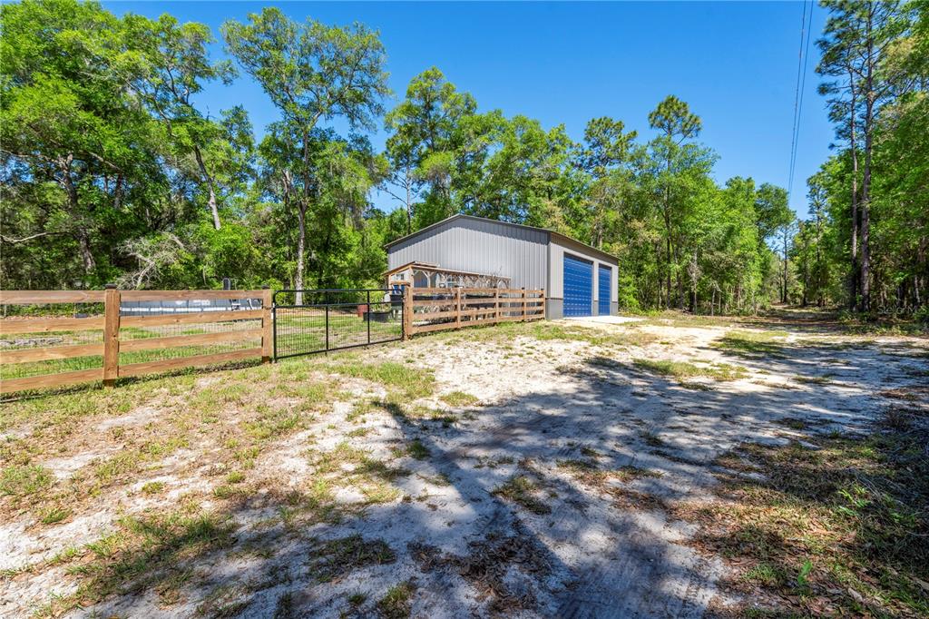 A metal workshop building stands behind a wooden fence on a sandy, wooded lot — 1886 STATE ROAD 20, HAWTHORNE, FL