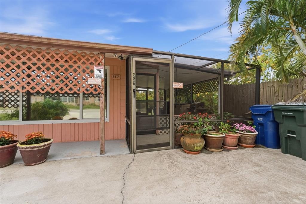 A concrete patio leads to a screened-in porch with potted plants and a pink exterior — 857 PALMETTO STREET, ENGLEWOOD, FL