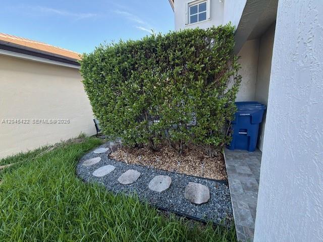A blue trash bin sits next to a hedge and a stone-bordered garden bed — 8277 NW 194th Ter # 2, Hialeah FL 33015, HIALEAH, FL
