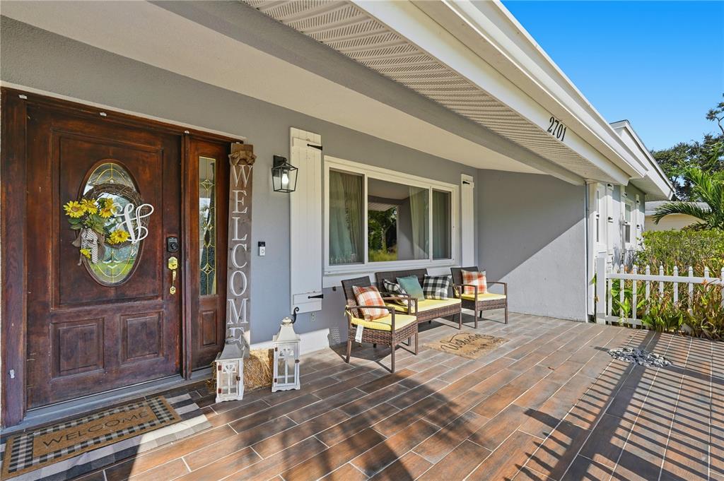 A covered front porch features wood-look tile flooring, a wooden door, and outdoor seating — 2701 64TH AVENUE S, ST PETERSBURG, FL