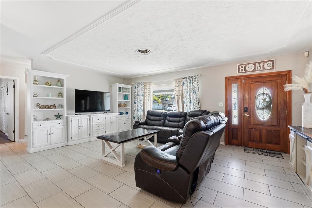 A living room features tile flooring, a dark leather sectional, and a wooden front door — 2701 64TH AVENUE S, ST PETERSBURG, FL