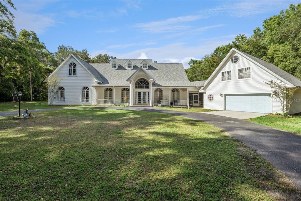 A large, white, two-story house with a sprawling lawn and an attached garage — 21033 VIOLET ROAD, BROOKSVILLE, FL