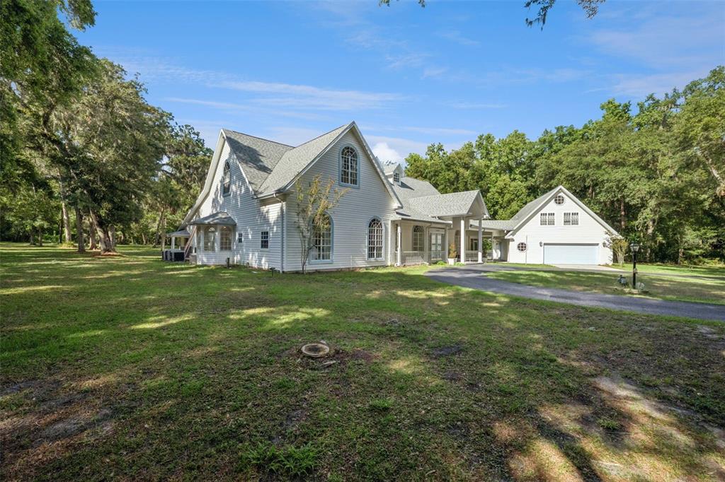 A white two-story house with a detached garage sits on a large, grassy, wooded lot — 21033 VIOLET ROAD, BROOKSVILLE, FL