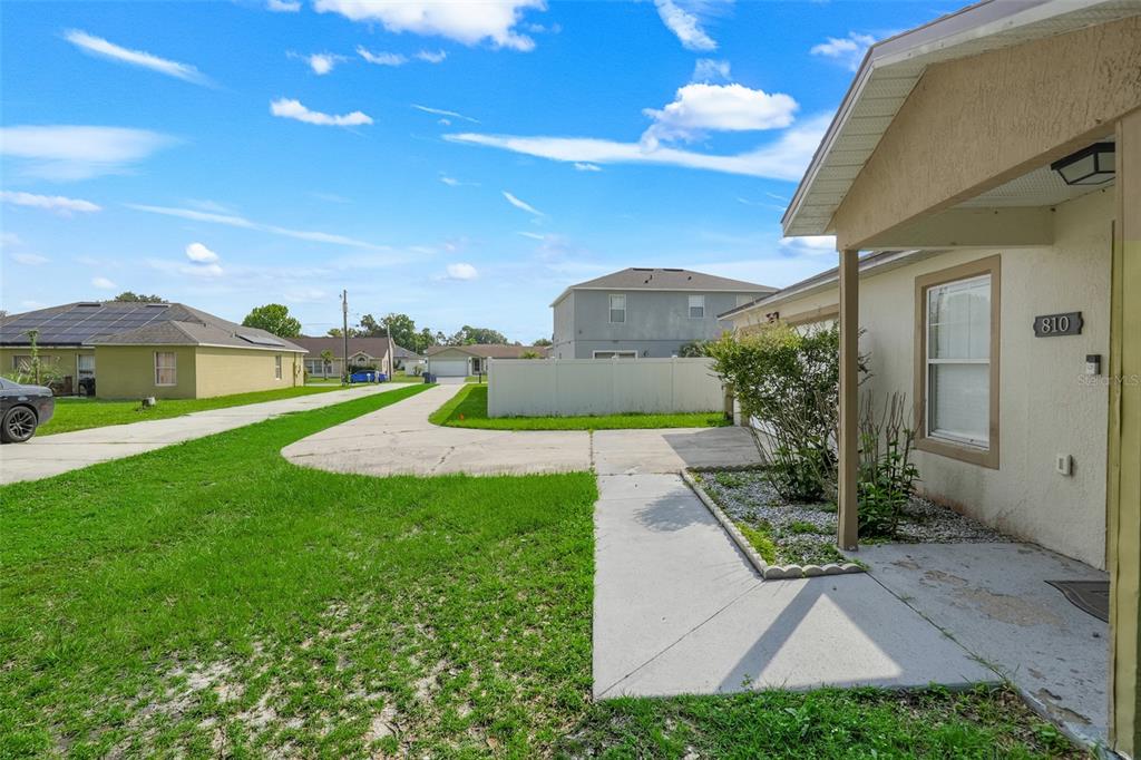 A view of a house exterior with a concrete driveway, lawn, and white privacy fence — 810 VALNERA COURT, KISSIMMEE, FL