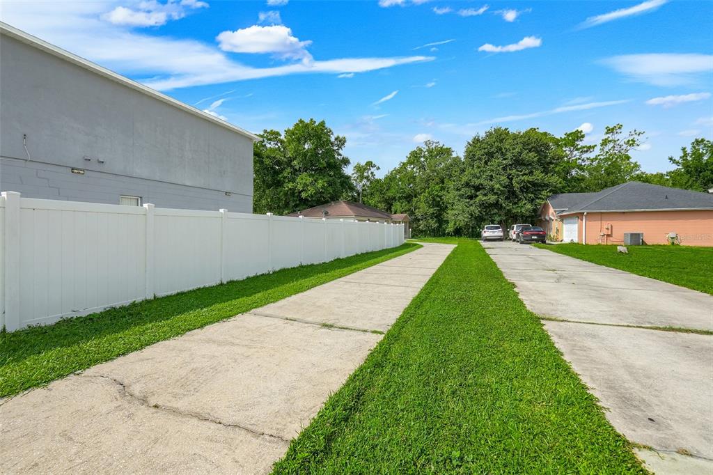 A long concrete driveway runs between a white vinyl fence and a peach-colored house — 810 VALNERA COURT, KISSIMMEE, FL