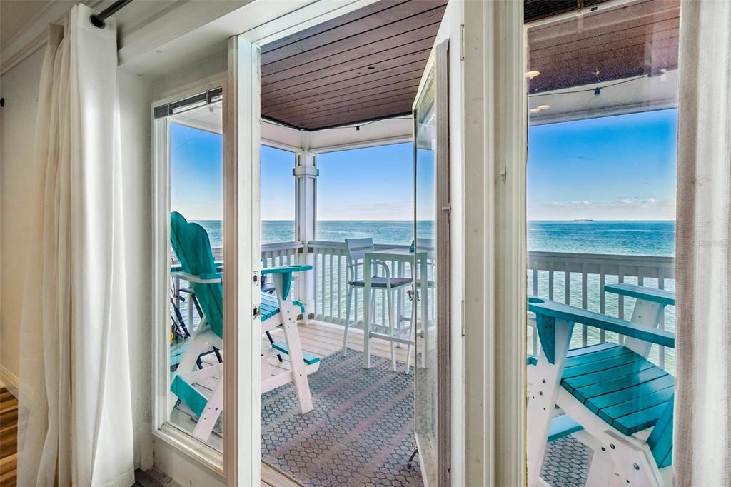 A view through open glass doors onto a balcony overlooking the ocean with patio furniture — 5110 COQUINA KEY DRIVE SE UNIT C, ST PETERSBURG, FL