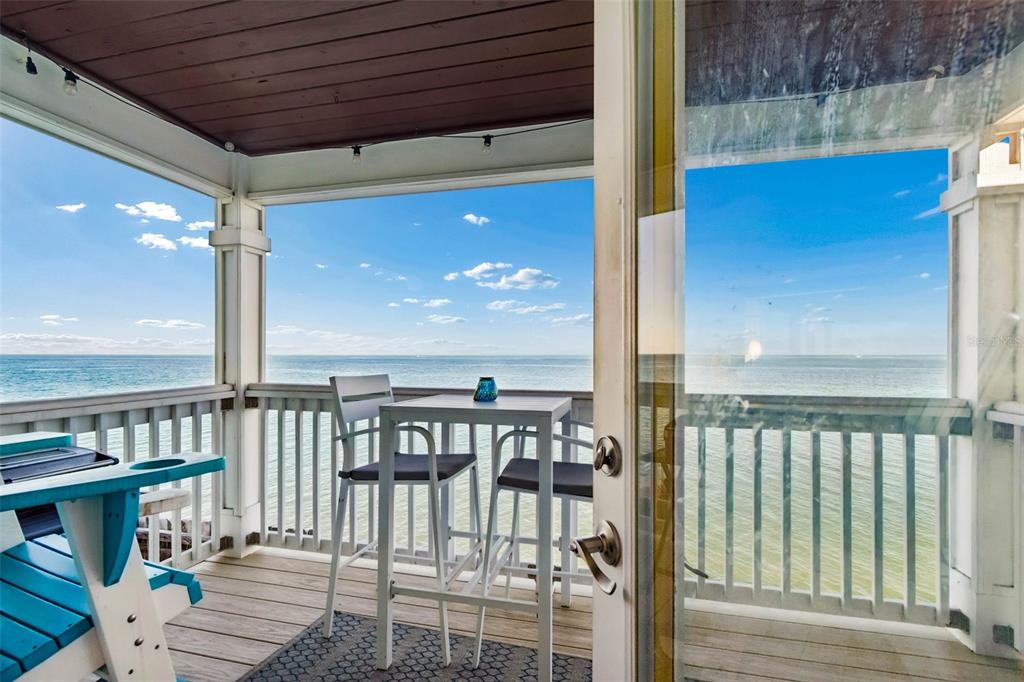 A covered wooden deck features a small table and chairs overlooking the ocean — 5110 COQUINA KEY DRIVE SE UNIT C, ST PETERSBURG, FL