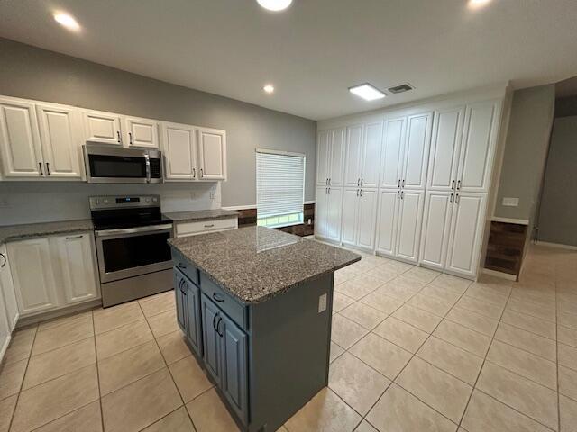 A kitchen features white cabinetry, a gray island with granite countertops, and light tile flooring — 1301 SW 83rd Avenue, Okeechobee FL 34974, OKEECHOBEE, FL