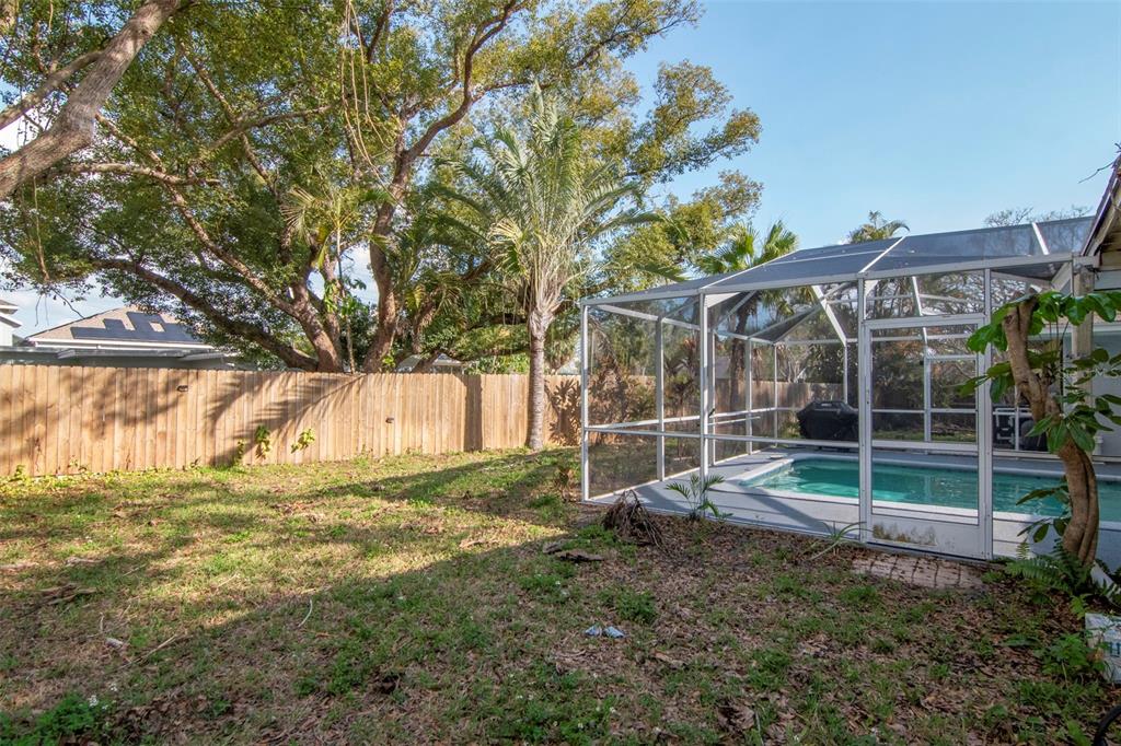 A backyard with a wooden fence, large trees, and a screened-in swimming pool — 347 COUNTRY CLUB DRIVE, OLDSMAR, FL