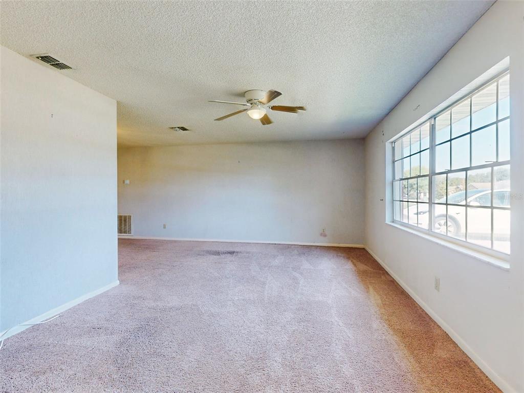 An empty room with beige carpet, a ceiling fan, and a large window — 1362 WOODBINE AVENUE, DELTONA, FL